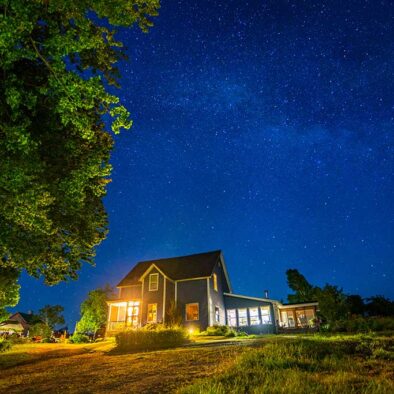 This image is an exterior shot of our Cape Breton Bed and Breakfast farmhouse. It is taken at night and the sky is filled with stars.